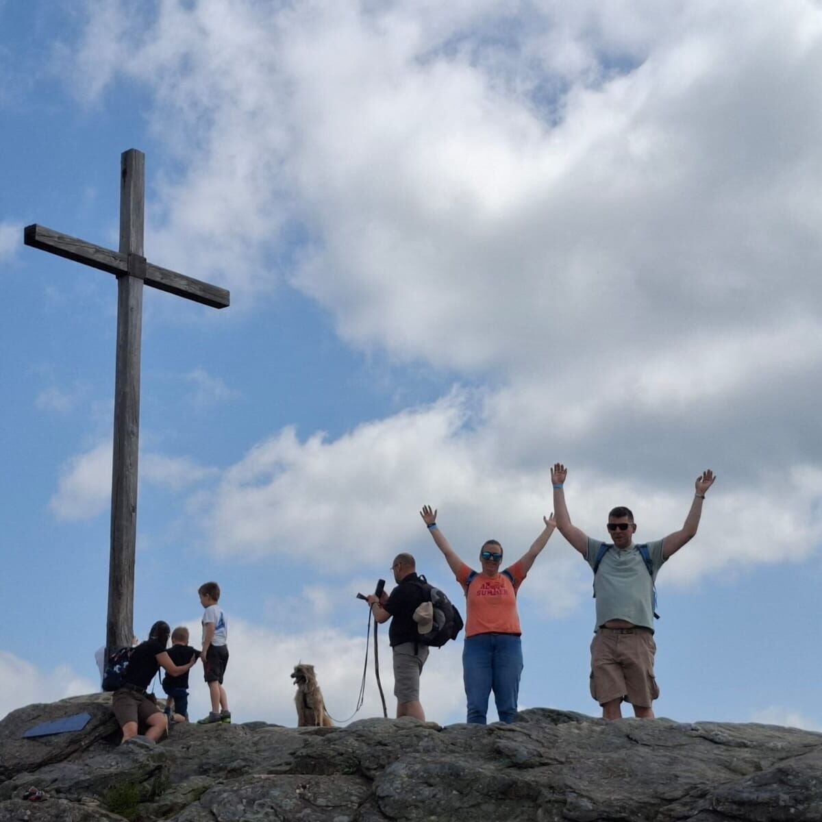 Sechs Menschen stehen auf einem Berg neben ihnen ist ein großes Holz Kreuz und ein Hund ist dabei.