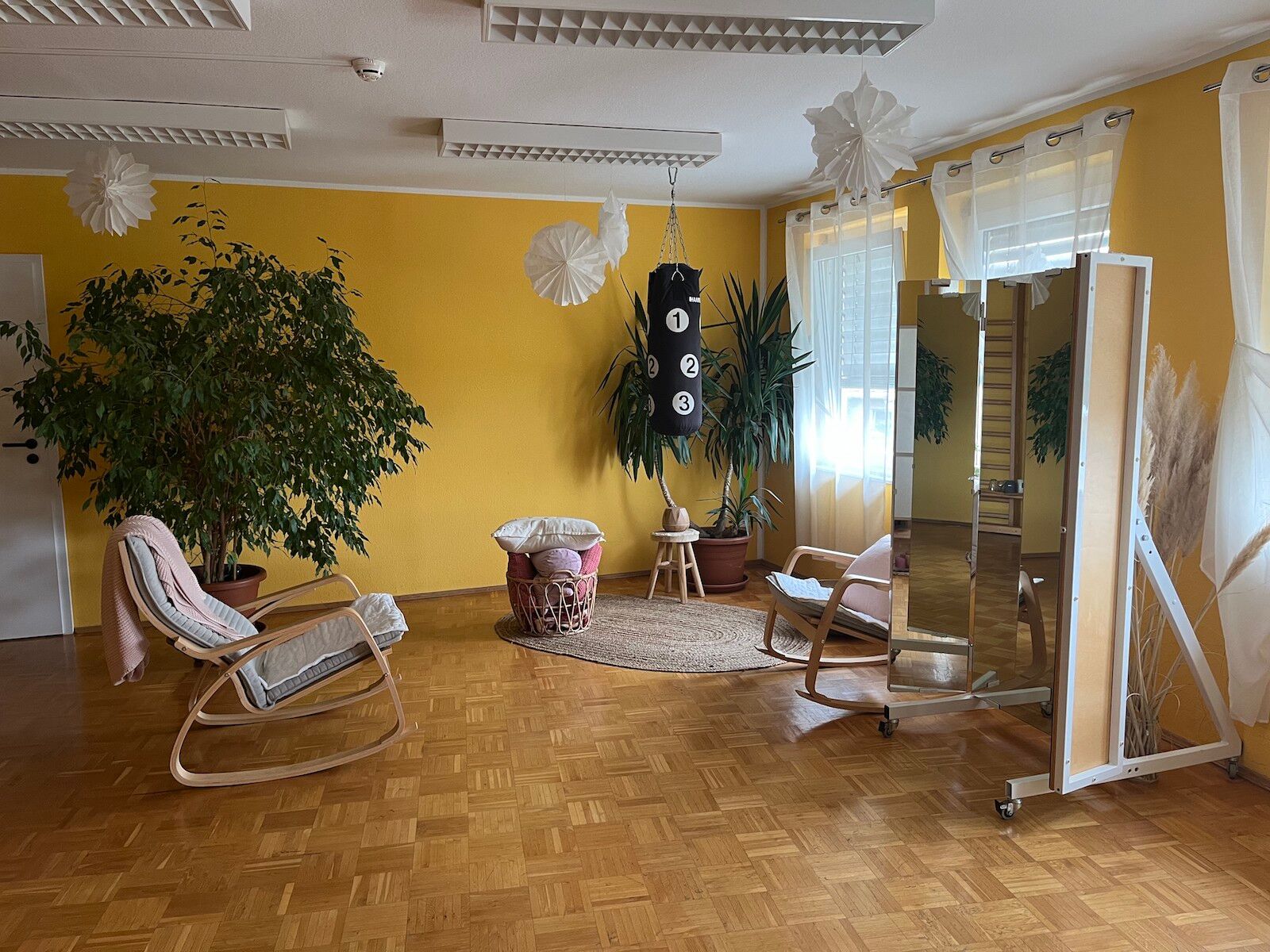 Die Sitzecke des Zimmers. Zwei Schaukelstühle, ein großer Spiegel, der Boxsack und mehrere Pflanzen.