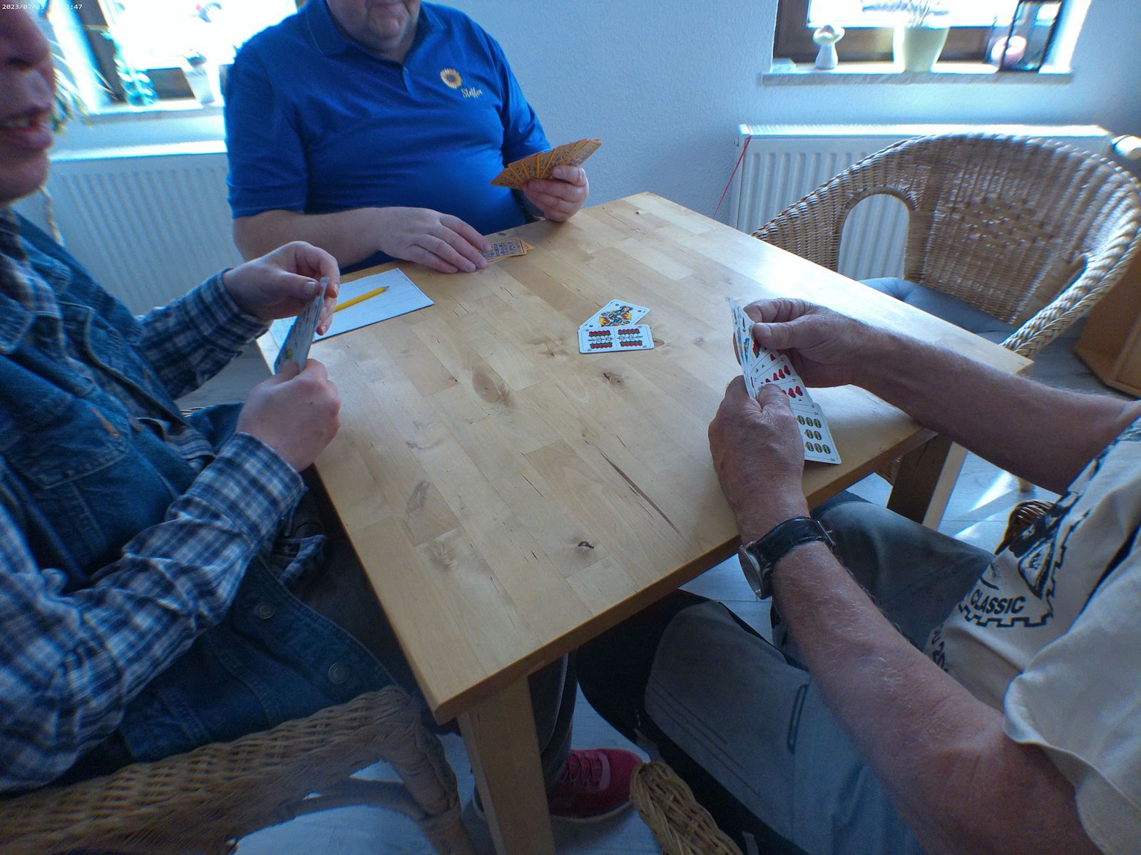 Einige Personen spielen gemeinsam ein Kartenspiel auf einem Holztisch.